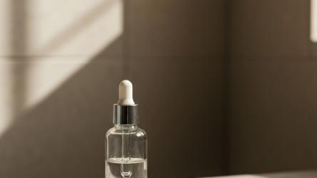 Hårvekst-serum med pipette på en lys steinbenk, mykt morgenlys