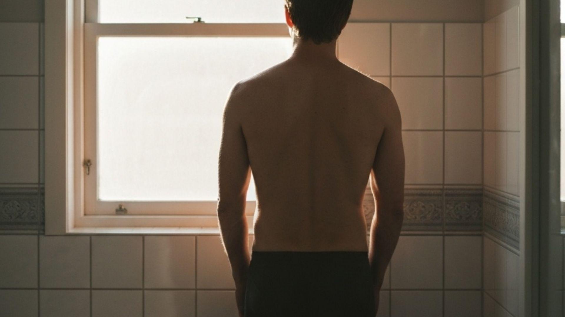 Mann ved et vindu i et minimalistisk bad, mykt morgenlys